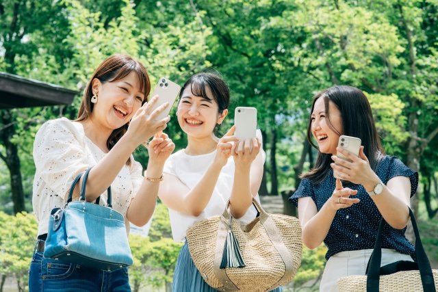 屋外でスマートフォンを使って撮影する3人の女性