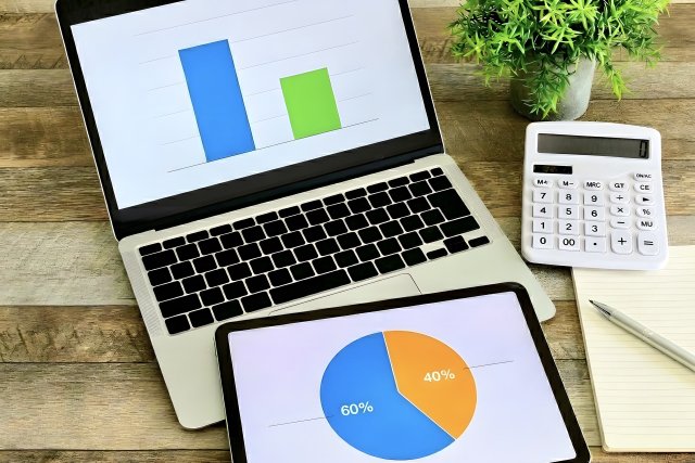 棒グラフを表示したノートパソコンと、円グラフを表示したタブレット、電卓
