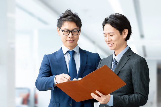 資料を見ながら話す2人のビジネスパーソン