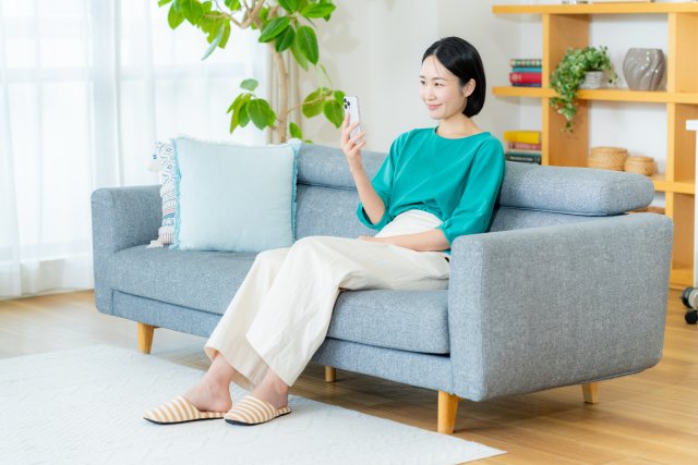 部屋のソファでスマートフォンを操作する女性
